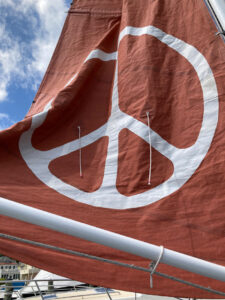 The Golden Rule sails are red the mizzen sail features a large white peace sign